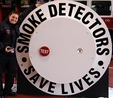 Fire Fighter Standing Next to A Giant Smoke Detect
